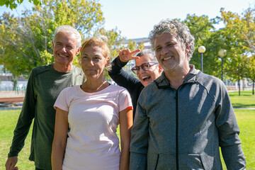 Cheerful excited sporty mature people standing together after morning exercises in park, looking away, smiling and laughing. Retirement or active lifestyle concept