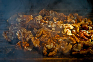 Walnut texture with steam close up. Many halves of peeled nuts on an old wooden board. Food in blue smoke on a background of shabby brown board. Contrasting dramatic light.