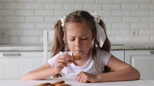 cute little girl eating cookie at home in kitchen. beautiful child eats cookies
