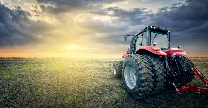 Fototapeta Agricultural tractor working in the field at sunset background