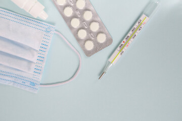 Medical mask, thermometer and medicines (pills) on a blue background
