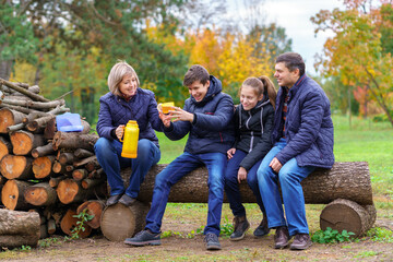 family relaxing outdoor in autumn city park, happy people together, parents and children, they drink tea, talking and smiling, beautiful nature