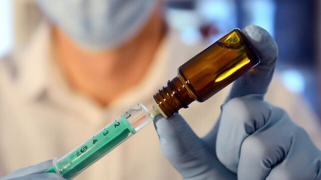 Researcher with face mask fills a syringe with medication. Filling a syringe with vaccine. Vial with vaccine. Biontech Pfizer Moderna Curevac Astrazeneca Novavax. Coronavirus vaccine.