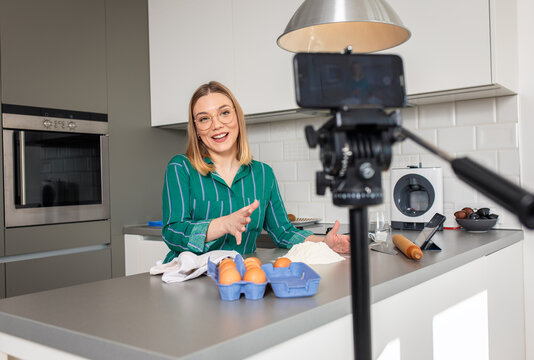 Young woman recording vlog at home in kitchen making croissants.