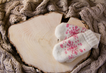 Obraz na płótnie Canvas Knitted white mittens with a pink snowflake lie on a wooden background. A knitted beige scarf is lying around. Copy space.
