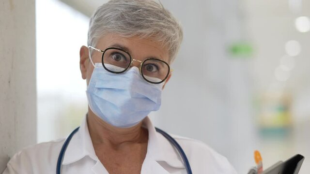Portrait of mature woman doctor standing in hospital hallway with face mask on