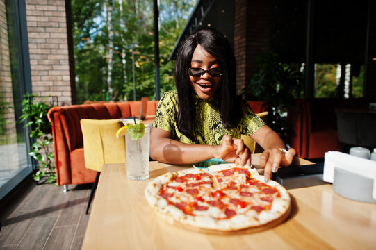 Glamour african american woman eating pizza at restaurant.