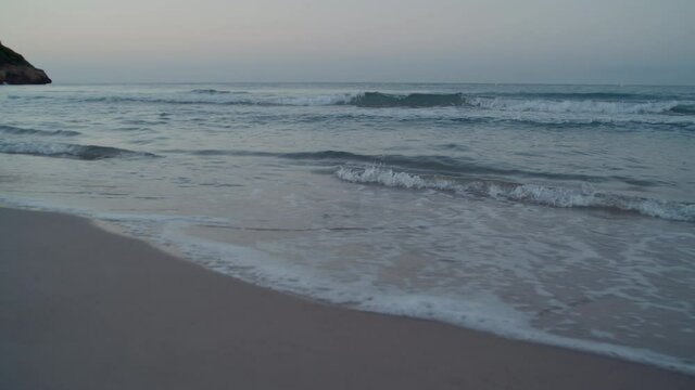 Static shot of calm ocean waves roll over shore, quiet and tranquil surf on sandy beach. 