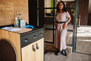 Fashion portrait of african american woman in long dress, boots and sunglasses indoor.