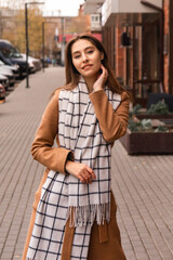 Fototapeta premium Young business woman in a light brown coat poses on the path near the house