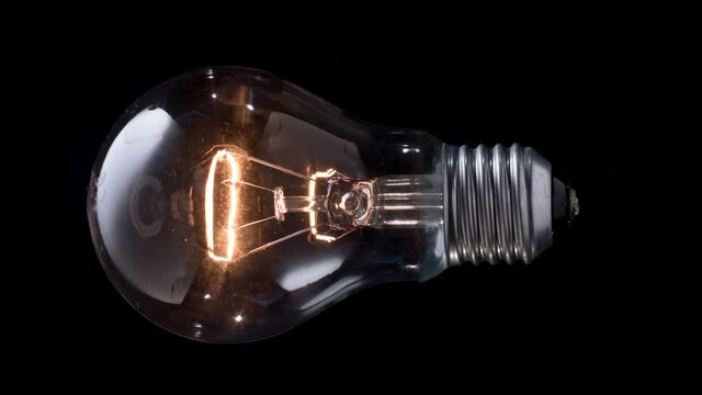 Light bulb glows on black background. New idea concept. Old type of incandescent light bulb turns on and off. Vertical stop motion video.