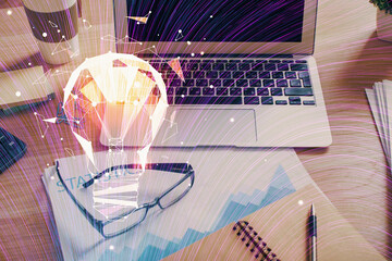 Computer on desktop in office with bulb icon hologram. Double exposure. Concept of idea.
