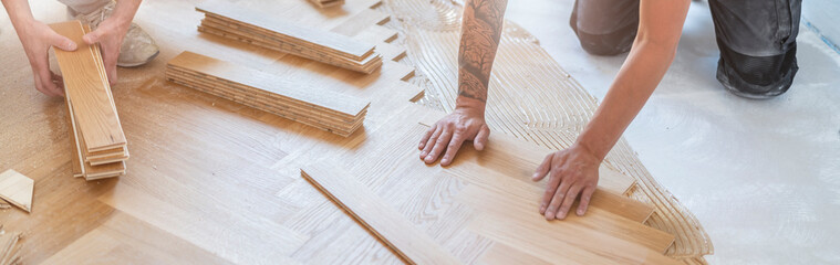 zwei Handwerker verlegen einen wunderschönen klassischen Holzboden auf einer Baustelle