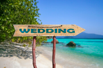 Wedding wooden arrow road sign against tropical beach with white sand and turquoise water background.