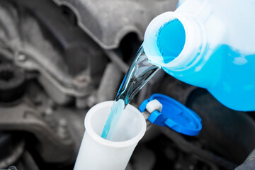 Pouring liquid from plastic canister into car washer fluid reservoir. Close up filling windscreen...