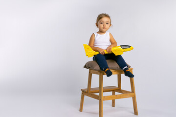 A cute little girl sits on a large stool with a yellow plane in her hands, posing. Gender...