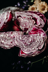Obraz premium red cabbage on a dining table covered with a black tablecloth. still life with cabbage and flowers in rustic style. making blaukraut. flowers and leaves of red cabbage on the table
