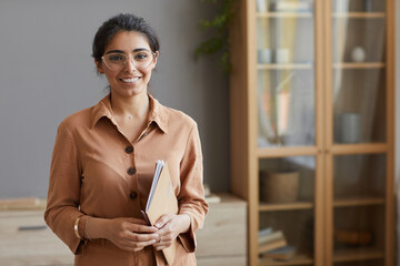 Portrait of young businesswoman in eyeglasses and in blouse holding folders and smiling at camera...