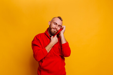 Happy  caucasian handsome brutal bearder man wearing warm red winter trendy fleece hoodie, studio shot, yellow background.   © Анастасия Каргаполов