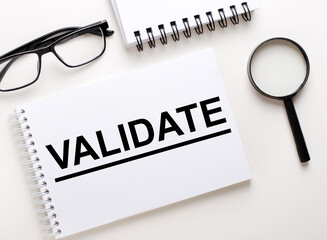 The word VALIDATE is written in a white notebook on a light background near the notebook, black-framed glasses and a magnifying glass.