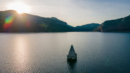 Pueblo sumergido en el pantano al atardecer, se ve la torre de la iglesia del pueblo
