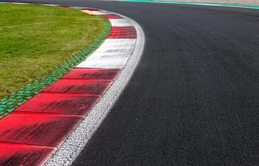 Fotobehang Close-up van de vuile stoeprand aan de linkerkant op een motorsportbaan met groen veld en zwart asfalt © fabioderby