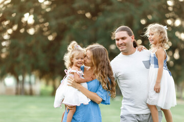 Parents hold daughters in their arms In Countryside, enjoing time together. Happy family concept. Blurred trees background in Sunset flare