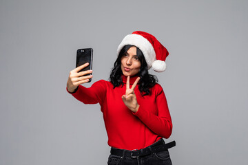 Naklejka premium Young pretty woman in santa hat take selfie on the phone isolated on gray background
