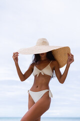 Fashion portrait of fit tanned slim stylish woman wearing large big giant straw hat on rocky...