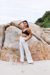 Portrait of happy slim stylish woman on rocky beach at sunset   