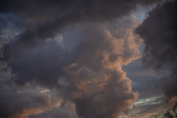 Silhouettes of epic stormy dark blue clouds with a gap of pink-orange light in a thunderstorm