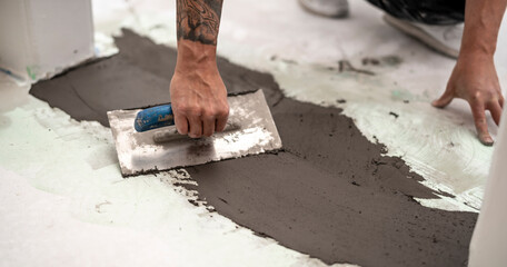 Parkettleger gleicht einen Höhenunterschied im Estrich aus, in dem er mit der Glättkelle schnelltrocknende standfeste Spachtelmasse aufzieht   © Anselm