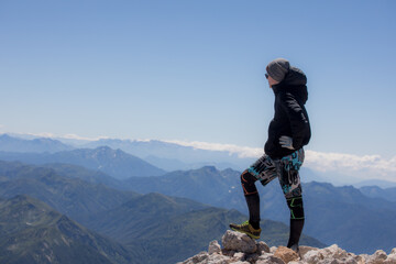 Young man at the top of the mountain admires the panorama of the mountains