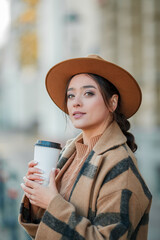 Beautiful young woman in a hat with coffee walks in a european city