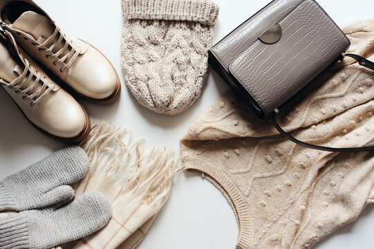 winter fashion set of woman clothes in neutral tones: warm sweater, hat, mittens, shoes and handbag on white background. Top view.