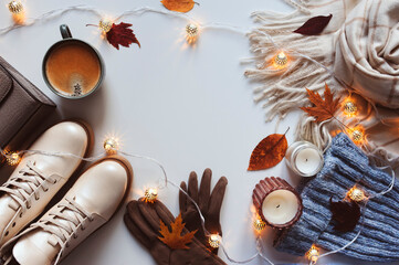 stylish modern winter or fall woman clothes set top view. Trendy shoes, sweaters and accessories in beige and blue tones with Christmas lights and autumn leaves.