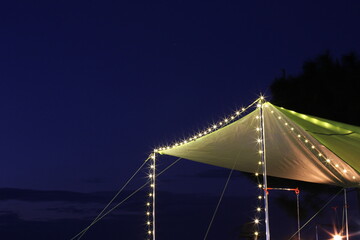 Fototapeta na wymiar Green roof tent lit at night with blue sky background