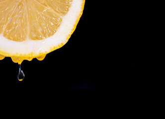 Close-up photo of front view of half a lemon on a black background with several drops of juice...
