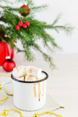 Hot chocolate with marshmallows and cinnamon in a white mug with drips on the background of a Christmas tree.