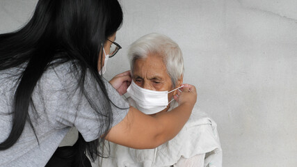 Asian grandchild woman wearing a white face mask to old grandmother prevent from covid 19. isolated concrete grey wall background. Rural lifestyle and health care concept.