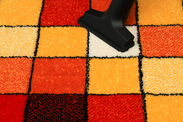Vacuuming a rug with a pattern of colored squares. Fluffy carpet, interior element, floor covering...