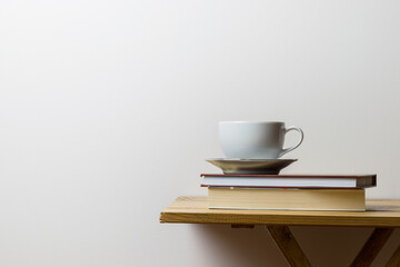 White cup of coffee on a book and on a wooden table, white background
