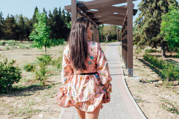Beautiful fashionable brunette woman in a dress with flowers walks in the park on the street