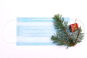 Medical protective mask on a white background.The mask is decorated with a fir branches and a little red gift box.New Year and coronavirus concept.Copy space, top view, flat lay.