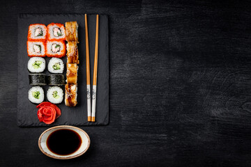 Japanese rolls on black slate board and black background top view, free space for text
