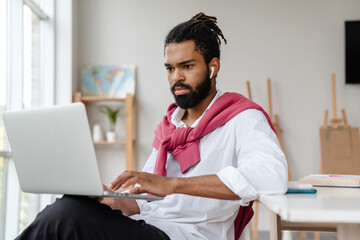 Serious african american guy in earphones working with laptop
