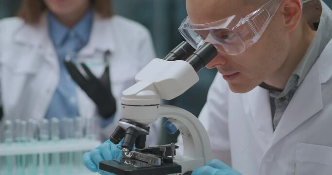 microbiologist is researching bacteria in laboratory, man is looking by microscope, biological research
