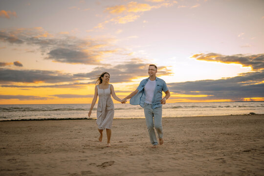 Happy couple running along the beach on sunset. . Image with selective focus.