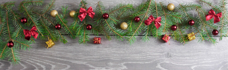 Wide Christmas border on wood, composed of green branches, red balls and ribbons, small giftboxes.