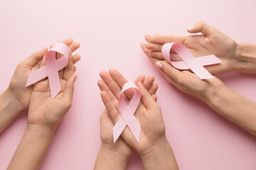 Female hands with pink ribbons on color background. Breast cancer awareness concept